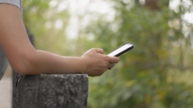 Kadın ellerinin gündelik kıyafet içinde cep telefonundan iletişim ve sosyal medyada sohbet için mesaj attığı fotoğrafları kapat. Güneş ışığı altında güzel doğal parktaki cep telefonunu kullanmak. Kablosuz teknoloji ve çevre kavramı. 