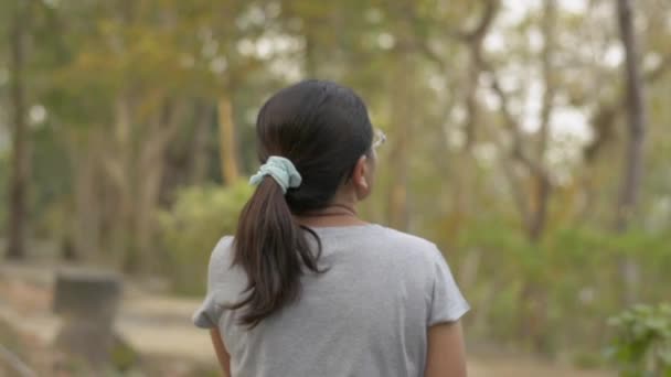夏の自然公園をのんびり歩いていると 眼鏡をかけたアジア人女性の背中からの眺め 後ろから追跡を閉じる スローモーション — ストック動画