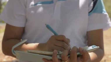 Yaz boyunca halka açık parkta günlük tutmak için yürüyen ve yazan bir kadın. Açık hava iş kaydı. Yavaş çekim.