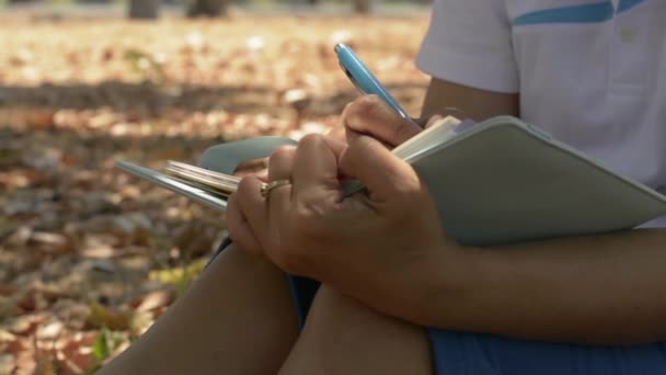 夏天的时候 女人坐在公园的树荫下写日志来激励自己的生活 室外工作录音 慢动作 — 图库视频影像