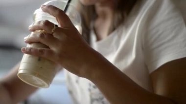 Asyalı bir kadın, kahve dükkanında bir bardak soğuk içecek içerken iletişim kurmak ve sosyal medyada sohbet etmek için cep telefonundan akıllı mesajlar atıyor..