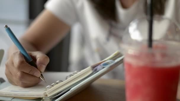 アジアの女性は人生を鼓舞し コーヒーショップでテーブルの上にスムージーフルーツジュースを飲むために日記に書いて — ストック動画