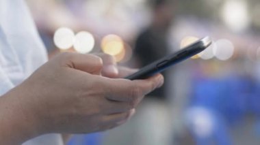 Cep telefonuyla iletişim kurmak ve sosyal medyada akşam yemeği pazarında sohbet etmek için mesaj atan bir kadının elleri. Bokeh arkaplanı ışıklandırılıyor.
