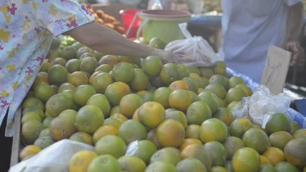 認識されていない人々は 地元の朝の市場でオレンジを購入して選択しています 農家の市場で老婦人の買い物オレンジ オレンジの山は プーケットの農業市場のベンダーによって販売されています — ストック動画