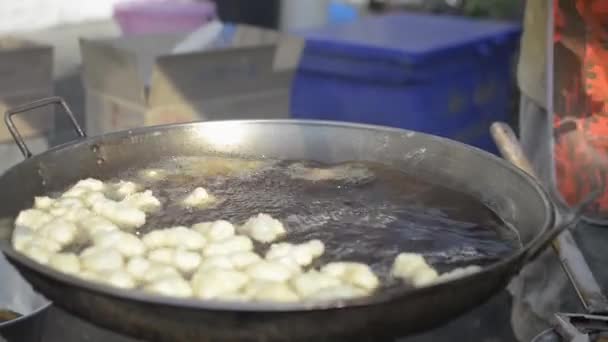 売り手は沸騰油で鍋に多くの小麦粉を入れています ストリートフード市場における泡状の油で揚げた生地スティック — ストック動画