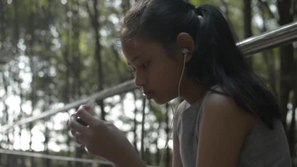 Asiática Linda Chica Usando Teléfono Móvil Con Auriculares Sentado Cerca — Vídeos de Stock