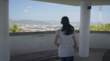 Sıradan giysili Asyalı tatlı kız görüş kulesine doğru koşuyor ve Pofet sahilinin yukarısındaki büyüleyici manzaranın keyfini çıkarıyor. Sevimli kız mutlu bir şekilde kollarını havaya kaldırıyor. Yavaş çekim.