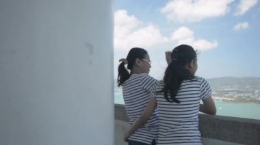 Anne ve kızı bulutlu mavi gökyüzü ile şehrin yukarısındaki güzel manzarayı izliyorlar. Anne ve kızı, Manzara Kulesi 'nde birbirlerine mutlu bir şekilde sarılıyorlar. Aşkın ifadesi. Yavaş çekimde döndürme.
