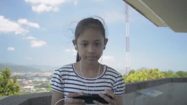 Asya 'lı genç bir kız kulaklıklı cep telefonundan müzik dinliyor ve yazın Phuket' te manzara kulesinde rahatça yürüyor..