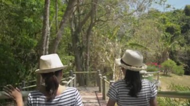 Anne ve kızı hasır şapka takıyor yaz boyunca doğal parktaki patikada el ele yürüyorlar..