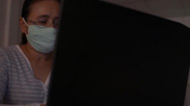 Koruyucu maske takan bir kadın evde dizüstü bilgisayarla masada çalışıyor. Coronavirus koruması. COVID-19 salgını. Sağlıklı ve güvenli yaşam kavramı. Döndürme atışı. Evden çalış..