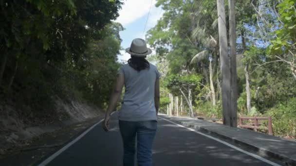 道をゆっくり歩く藁帽子をかぶったアジアの女性の背面図 夏の間 田舎の常緑樹の美しさを見ている女性自然保護主義者 スローモーションで撮影した後 — ストック動画