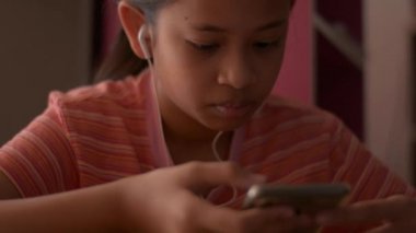 Evde internet medyasını izlerken kulaklıkla cep telefonu kullanan Asyalı küçük kız. Eğlence için iletişim.