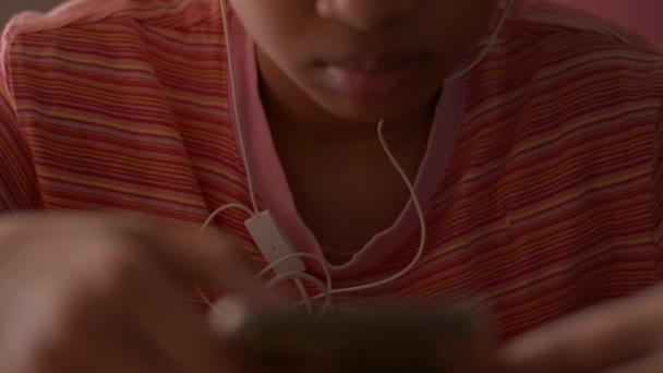 自宅でオンラインメディアを見ながらイヤホンで携帯電話を使うアジア系の少女 娯楽のためのコミュニケーション — ストック動画