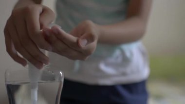 Asyalı tatlı kız ellerini alkol jeliyle temizliyor ve COVID-19 salgını sırasında yatak odasında cep telefonu kullanmadan önce koruyucu maske takıyor. Coronavirus koruması. 