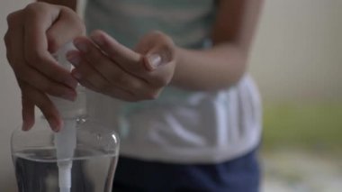 Asyalı tatlı kız ellerini alkol jeliyle temizliyor ve COVID-19 salgını sırasında yatak odasında koruyucu maske takıyor. Coronavirus koruması. 
