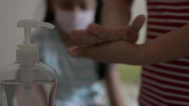 Anne ellerini alkol jeliyle temizliyor ve yaklaşmadan önce koruyucu maske takıyor ve COVID-19 salgını sırasında kızına sarılıyor. Coronavirus koruması. 