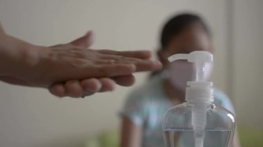 Anne ellerini alkol jeliyle temizliyor ve yaklaşmadan önce koruyucu maske takıyor ve COVID-19 salgını sırasında kızıyla oynuyor. Coronavirus koruması. 