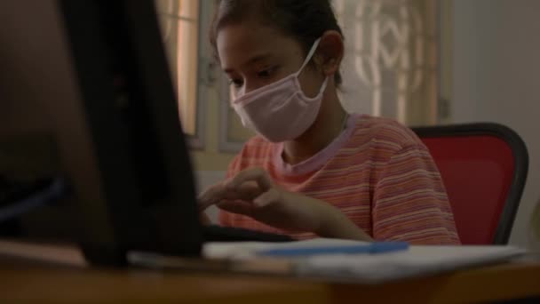 在Covid 19疫情爆发期间 一个戴着防护面具 带着电脑在家里写字台的可爱女孩 家庭概念研究 — 图库视频影像