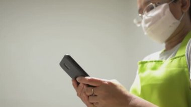 Ev hanımı koruyucu maske takıyor cep telefonundan mesaj atıyor ve evdeki sosyal medyada sohbet ediyor. Covid-19 durumu sırasında veri takibi ve cep telefonuyla günlük haberler.