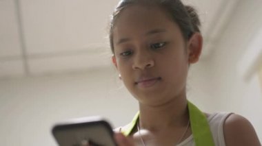 Önlüklü Asyalı tatlı kız evde arkadaşıyla mutlu bir şekilde çevrimiçi iletişim kurmak için cep telefonu kullanıyor. Gülümseyen genç kız cep telefonundan sosyal medyayla sohbet ediyor.