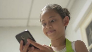 Önlüklü Asyalı tatlı kız evde arkadaşıyla mutlu bir şekilde çevrimiçi iletişim kurmak için cep telefonu kullanıyor. Gülümseyen genç kız cep telefonundan sosyal medyayla sohbet ediyor.