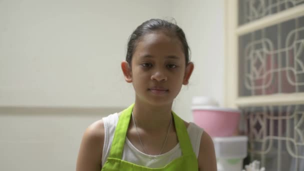 一个穿着围裙笑着的可爱女孩在厨房里拿着食物载体和铲子的形象 快乐的少女厨师 家里有厨房用具 — 图库视频影像