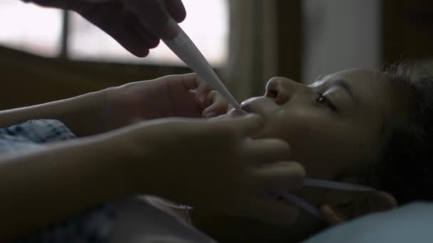 Covid 19の状態で温度計を使用して温度を測定してベッドの上に寝そべって病気の娘の世話をする母親の手 コロナウイルス対策 健康と安全のライフコンセプト — ストック動画