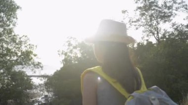 Sırt çantalı, hasır şapkalı tatlı Asyalı kız ellerini kaldırıyor ve gün batımında mangrov ağaçlarıyla sahilin güzel manzarasını seyretmekten zevk alıyor. Yavaş çekim.