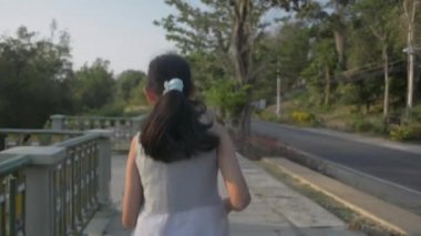 Neşeli Asyalı hoş bir kız günbatımında Pofet 'te mangrov ağaçlarıyla sahilin güzel manzarasını izlerken koşuyor ve ellerini havaya kaldırıyor. Yavaş çekim.
