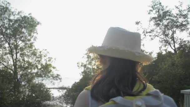 かわいいアジアの女の子は バックパックを歩くと 夕暮れ時にマングローブの木と海岸の美しい景色を楽しむ空気に手を上げわら帽子を身に着けています — ストック動画