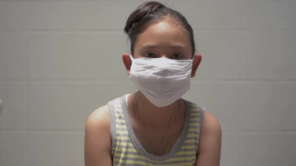 ポートレートアジアのかわいい女の子は家に滞在中に保護マスクを脱ぐ シングルシャツを着た女性のティーンエイジャーは カメラを見て深く息をし コロナウイルス対策 — ストック動画