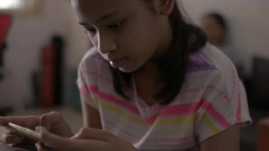 Asyalı şirin kız cep telefonuyla oyun oynuyor ve evde karantina sırasında annesinden uzakta oturuyor. Annenin cep telefonunu kullanıp oturma odasındaki kanepeye oturmasını engelle. Sosyal uzaklık kavramı. 