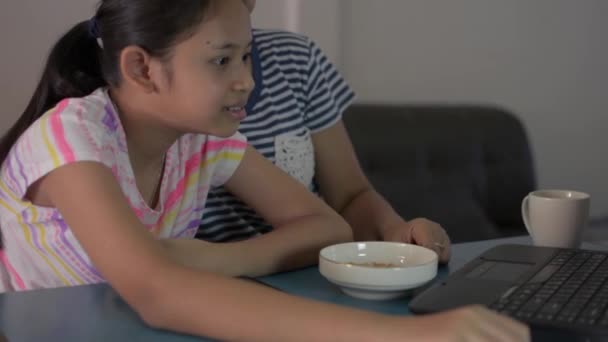 宿題をしている間にラップトップからオンラインでレッスンを見ている彼女の母親とアジアのかわいい女の子 母はCovid 19パンデミックの状況の間にビデオ通話で家からの彼女の娘の研究を助け 教える 家から学ぶ — ストック動画