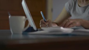 Kadın hesap bakiyesini kontrol ediyor ve evdeki oturma odasında harcamaları hesaplıyor. Ev hanımı hesap makinesiyle çalışıyor ve karantina sırasında COVID-19 salgınıyla birlikte masaya not alıyor. Evden çalışıyorum. Döndürme çekimi.