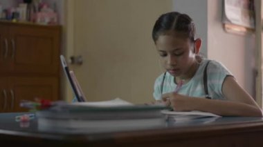 Güzel Asyalı kız kulaklık takıyor ve dijital tableti evde ders olarak kullanıyor. Kadın öğrenci COVID-19 salgını sırasında video ile evden ders çalışıyor..