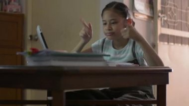 Kulaklık takan sevimli kız evdeki dijital tabletten ders izlerken eğlenceli jestler yaparak rahatlıyor. Kadın öğrenci COVID-19 salgını sırasında video ile evden ders çalışıyor..