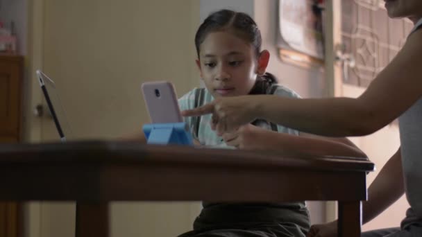 可爱的女孩和她的母亲在做家庭作业的过程中通过手机在线观看课程 Covid 19大流行期间 母亲通过视频电话帮助和教育女儿在家学习 — 图库视频影像