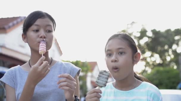 美少女と妹は 住宅街の夏の日差しの下 歩道に立ちながらアイスクリームを食べるのを楽しんでいます 友情だ スローモーション — ストック動画