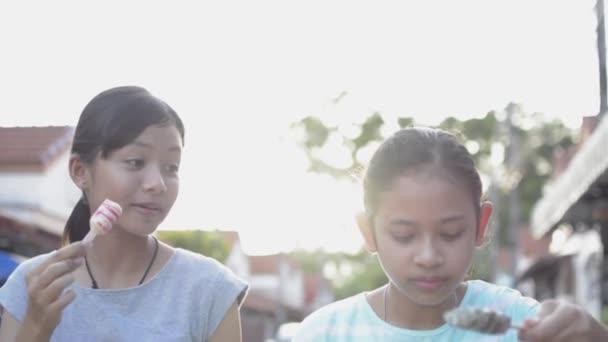 两个女孩喜欢夏天在屋檐下的小径上一起在阳光下散步时吃冰淇淋 慢动作 — 图库视频影像