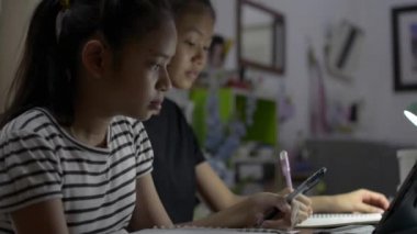 İlkokul kızları evde online ders için dijital tablet kullanıyorlar. COVID-19 salgını sırasında evden video araması yaparak kitap yazan iki genç kız..