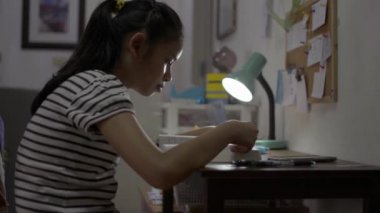 Asyalı tatlı kız evde karantina sırasında masada bir roman okuyor ve sayfaları çeviriyor. Liseli kız sınav için geceleri masanın üstünde bir kitapla ders çalışıyor..