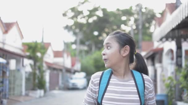バックパック付きの面白い女の子の肖像画は 住宅街の歩道に立っている間に興奮した表情を示しています 顔の表情 — ストック動画