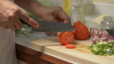 Ahşap kesme tahtasında bıçakla domates doğrayan kadın şef. Mutfaktaki masada baharatlı salata için malzeme hazırlayan kadın ellerini kapat. Yavaş çekim çekim..