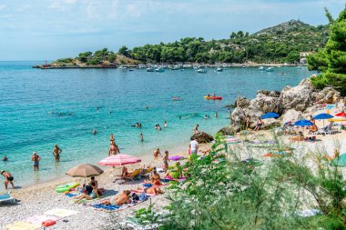 MLINI, CROATIA - 6 AĞUSTOS 2016: Mlini, Dubrovnik yakınlarında insanların turkuaz suda yüzdüğü ve kumlu sahilde güneşlendiği bir tatil beldesi.