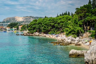 MLINI, CROATIA - 6 AĞUSTOS 2016: Mlini, Dubrovnik yakınlarında insanların turkuaz suda yüzdüğü ve kumlu sahilde güneşlendiği bir tatil beldesi.