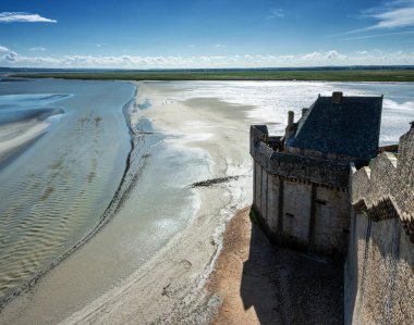 Fransa, Normandiya 'da Mont Saint-Michel adlı manastırın yakınındaki çamur düzlüğü, İngiliz Kanalı kıyıları, insanlar kumsalda yürüyor, yazın güneşli bir gün, mavi gökyüzü arka planı.