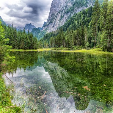 Dachstein dağları, ormanlar, bulutlar ve Avusturya Alpleri 'ndeki sulardaki yansımalarla güzel Gosausee gölü manzarası. Salzkammergut bölgesi.