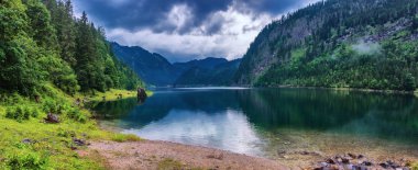 Dachstein dağları, ormanlar, bulutlar ve Avusturya Alpleri 'ndeki sulardaki yansımalarla güzel Gosausee gölü manzarası. Salzkammergut bölgesi.