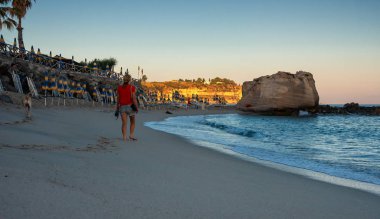 Sabahın erken saatlerinde Tropea 'nın boş sahillerinde yürüyen bir kadın.